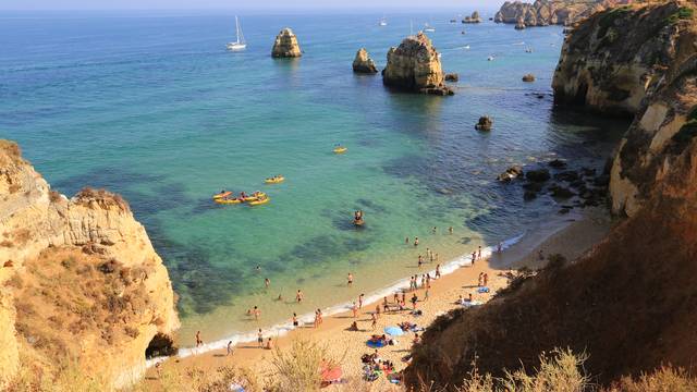 Klippenküste mit klarem Wasser, Badenden und Booten